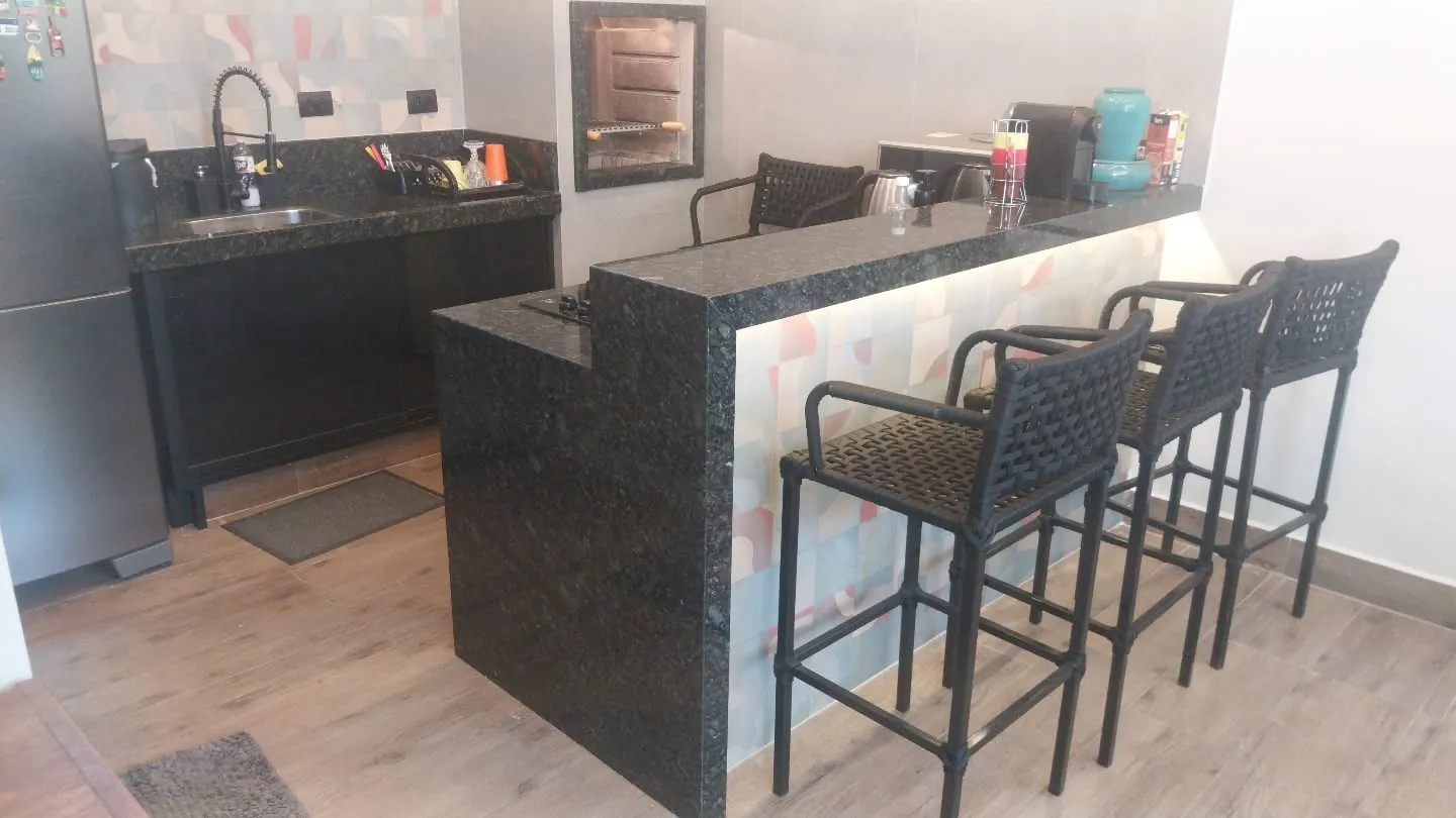 Cozinha com pia e balcão em granito verde e banquetas
